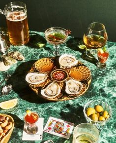 a table topped with oysters and glasses of beer next to plates of food on top of it