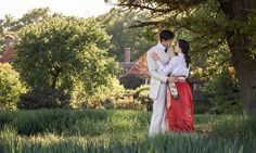 a man and woman standing next to each other under a tree in the middle of a field