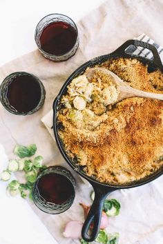 a skillet filled with food next to glasses of wine