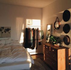 a bedroom with clothes hanging on the wall and a dresser in front of it, next to a bed