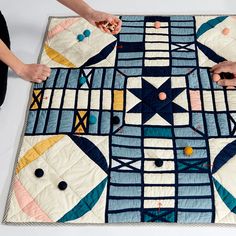 two people are making a quilt on the floor with scissors and thread, while another person is holding something in their hand