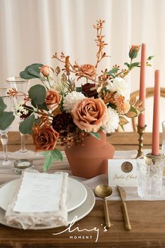 an arrangement of flowers in a vase on a dining room table with place settings and napkins