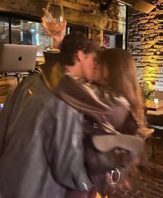 a man and woman kissing in front of a laptop computer on a table next to a brick wall