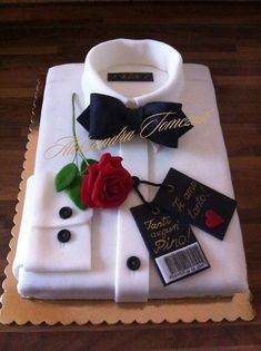 a white shirt with a red rose and black bow tie on it is sitting on top of a wooden table