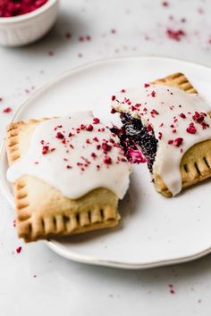 two pastries with white icing and red sprinkles on a plate