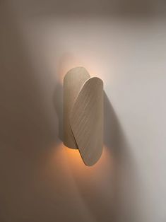 a white wall light with a curved wooden design on it's side and an orange light at the end