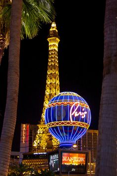 the eiffel tower lit up at night with palm trees in front of it