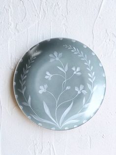 a plate with flowers painted on it is hanging on the wall in front of a white brick wall