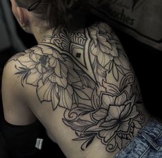 a woman's back tattoo with flowers on her upper arm and shoulder, in black ink