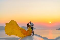 a man and woman standing on top of a roof next to the ocean at sunset