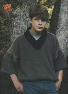 a young man standing in front of a tree