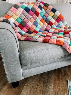 a multicolored crocheted blanket sitting on top of a gray couch in a living room