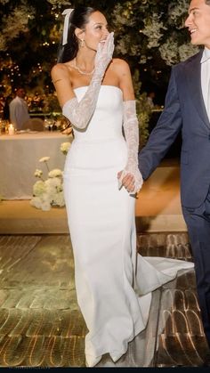 a bride and groom holding hands walking down the aisle at an outdoor wedding reception with lights in the background