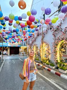 a woman standing in the middle of an empty street with lots of colorful paper lanterns hanging above her