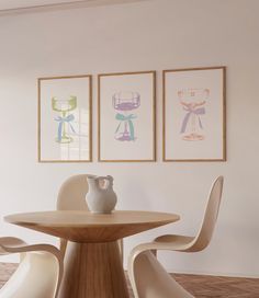 three framed pictures hang on the wall next to a table with two chairs and a vase