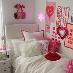 a white bed topped with lots of pink and red pillows next to a wall covered in pictures