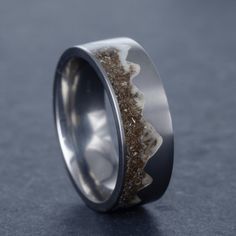 a wedding ring with sand and silver inlays on the inside, against a dark background