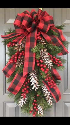 a red and black wreath with pine cones, berries and evergreens hanging from the front door