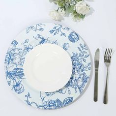 a white plate with blue flowers on it next to silverware and a flower arrangement