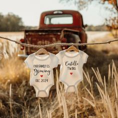 two baby onesuits hanging on a clothes line in front of an old truck