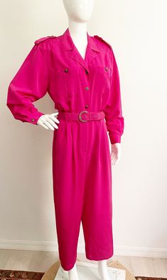 This is a bright pink long sleeved jumpsuit from Chaus.  It has a  nod to military styling and a matching belt.  Buttons down the front and zipper at pant section.  Two side pockets.  The elastic at the waistband has lost its stretch.  Still very wearable.  Size tag 10, polyester, washable. Measurements taken with jumpsuit laying flat and doubled where appropriate. In order to determine fit we recommend comparing measurements with an item that fits you well. Length 55 inches Underarm to underarm Solid Belted Jumpsuits And Rompers For Fall, Fall Solid Color Belted Jumpsuits And Rompers, Belted Long Sleeve Jumpsuits For Work, Belted Long Sleeve Jumpsuits And Rompers For Work, Vintage Long Sleeve Jumpsuits And Rompers For Work, Vintage Long Sleeve Jumpsuit For Work, Belted Long Sleeve Jumpsuits For Spring, Belted Long Sleeve Jumpsuits And Rompers For Spring, Vintage Long Sleeve Jumpsuits And Rompers For Fall