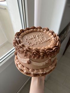 a person holding a cake with the words happy birthday on it in front of a window