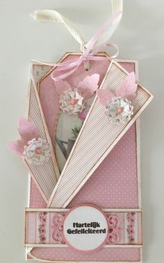 a pink card with flowers and ribbons on it's side, in a box