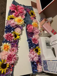 a pair of jeans with flowers on them sitting next to a sewing machine and computer