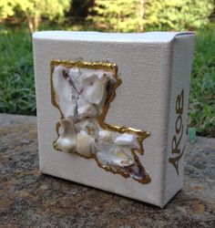 a white box sitting on top of a rock covered in gold leafy paint and shells