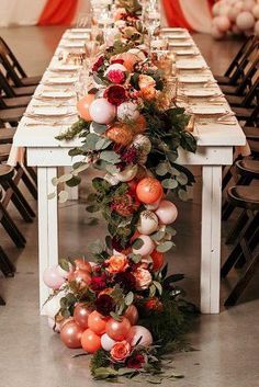 a long table is decorated with orange and pink flowers, greenery, and candles