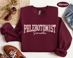 a maroon sweatshirt with the words phlebotomist on it next to some shoes and sunglasses