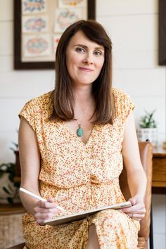 a woman sitting on a chair holding a book in her hands and looking at the camera