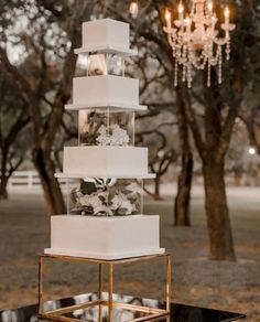 a tall white cake sitting on top of a black table under a chandelier