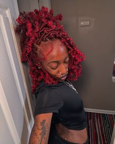 a woman with red dreadlocks and tattoos on her body standing in a doorway