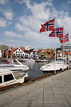 several boats are docked in the water with flags flying from them and buildings on either side