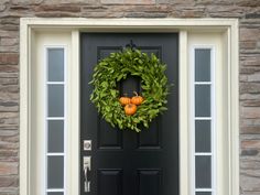 a black front door with a green wreath and two pumpkins on the top one