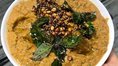 a white bowl filled with soup and topped with spinach leaves, seeds and nuts