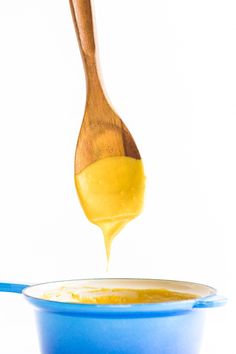 a wooden spoon is pouring liquid into a blue bowl with yellow liquid in it on a white background