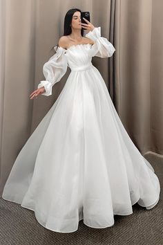 a woman taking a selfie wearing a white wedding dress with long sleeves and flowing ruffles