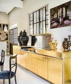 an elegant kitchen with gold cabinets and black vases on the countertop, along with two chairs