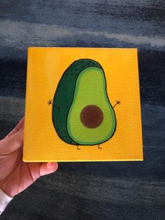 an avocado painted on a piece of yellow paper in someone's hand