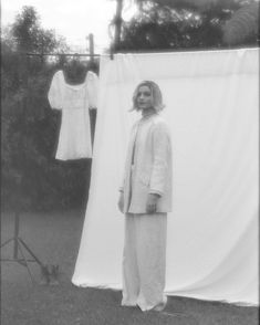 black and white photograph of woman standing in front of clothes hanging on a line outside