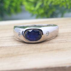 a silver ring with a blue stone in the center on a wooden table next to green plants