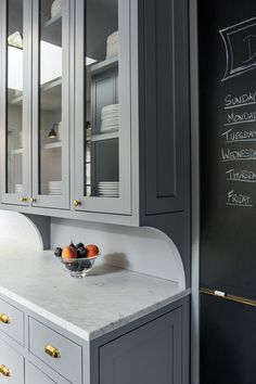 a kitchen with gray cabinets and marble counter tops, chalkboard on the wall behind it