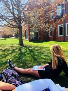 two people sitting on the grass in front of a building