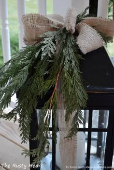 a lantern decorated with evergreen and burlap ribbon on the front porch for christmas