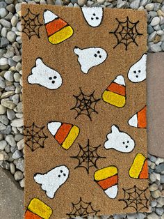 a halloween door mat with ghost, pumpkins and candy corn on it next to some rocks