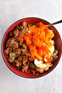 a bowl filled with meat and vegetables on top of a white countertop next to a spoon