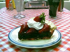 a piece of chocolate cake with whipped cream and strawberries on top sits on a checkered tablecloth