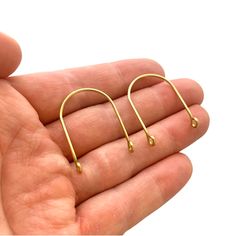 a hand holding a pair of small gold ear clips in their palm, with the end of